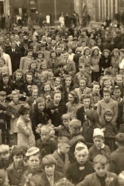 Zwartwitfoto van een grote menigte volwassenen en kinderen, vele met een strik in hun haar.