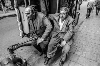 Twee mannen in pak zitten achter het stuur van een draaiorgel.