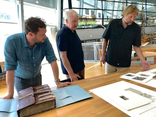 Drie mannen staan achter een tafel met archiefstukken.