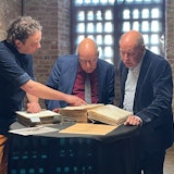 Drie mannen bekijken een oud archiefstuk.