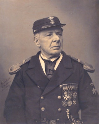 Een man met een pet en onderscheidingen op zijn uniform kijkt schuin opzij.