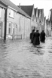 Drie mannen op de rug gezien lopen tot hun dijen toe in het water in een straat.