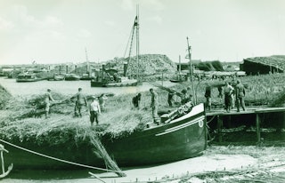 Arbeiders staan op schepen geladen met materialen voor het bouwen van een dam.