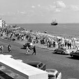 Boulevard, strand en zee Vlissingen. Op de voorgrond badgasten en auto's, op de achtergrond een voorbijvarend schip.