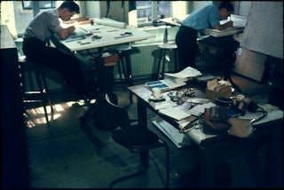 Rommelig kantoor waar twee jongemannen aan tekentafels werken.