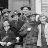 Een groep soldaten, mannen, vrouwen en kinderen poseert en lacht naar de fotograaf.
