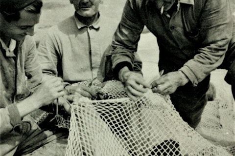 Drie mannen werken aan een visnet.