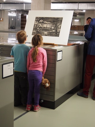 Twee kinderen kijken aandachtig naar een prent die op een archiefkast staat.
